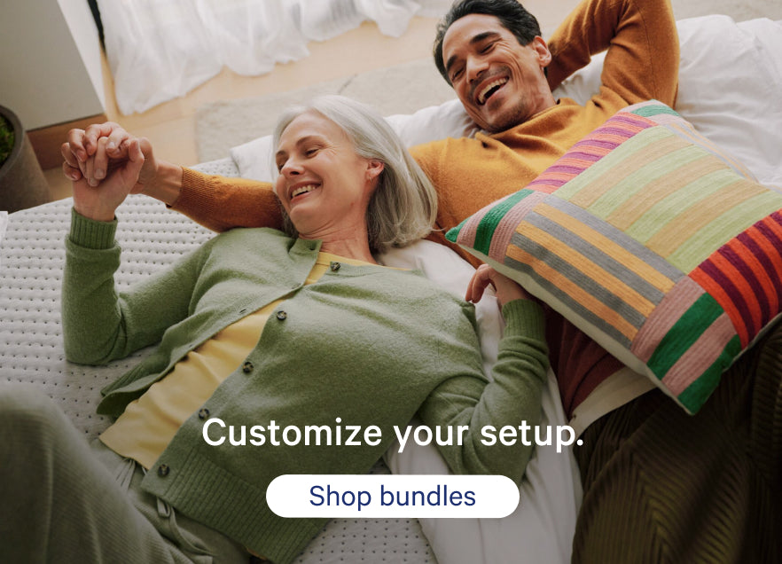 A couple lies back on their mattress smiling. Promotional text on the image says, "Customize your setup. Shop bundles."