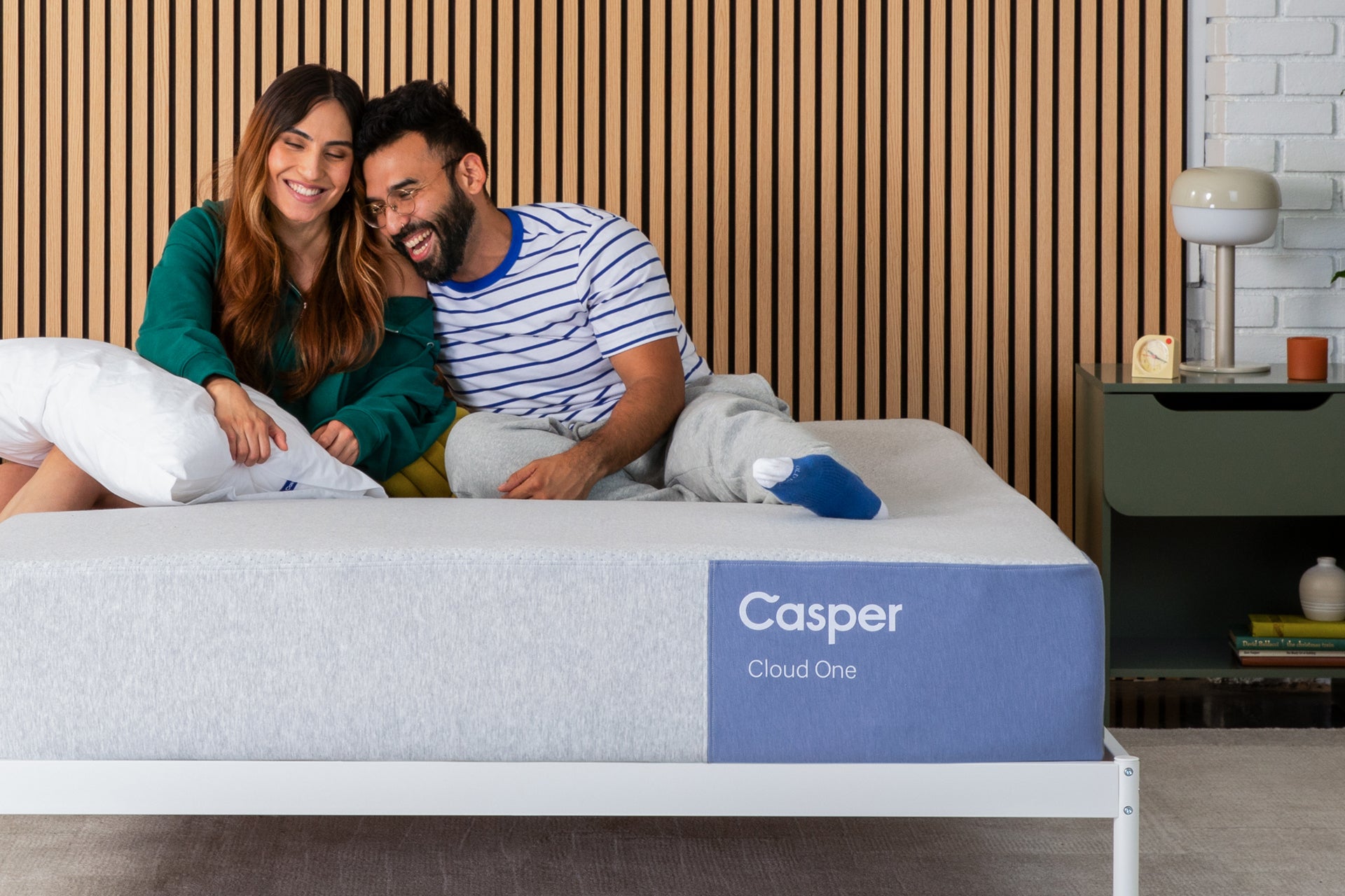 A couple sits together and smiles on their Cloud One mattress in a bedroom