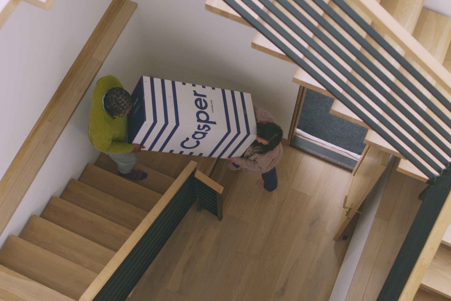 A video of a couple carrying their new Casper mattress in its box up the stairs to their bedroom, then lying in bed and smiling.