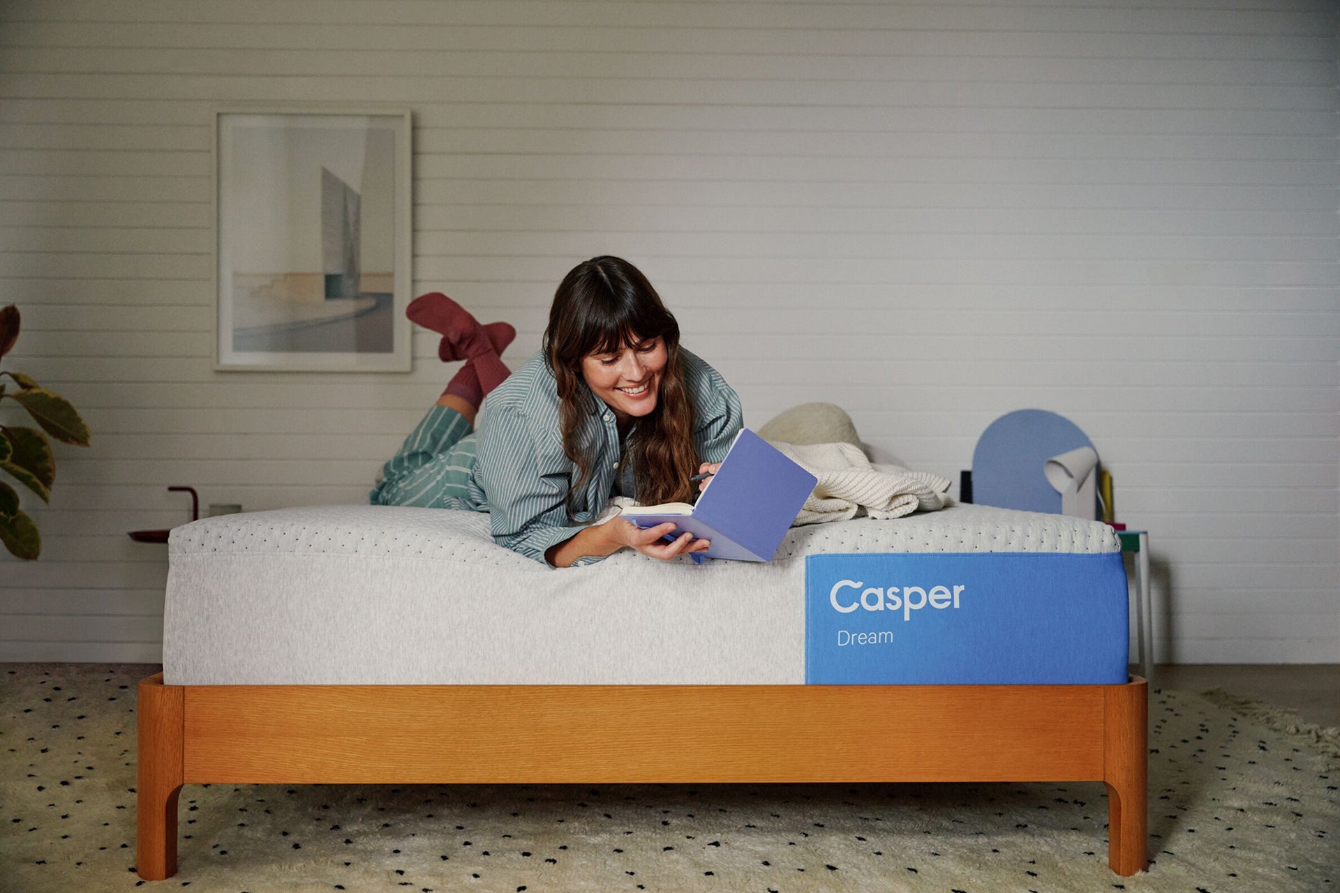 A woman lies near the edge of her Casper Dream mattress writing in a book.
