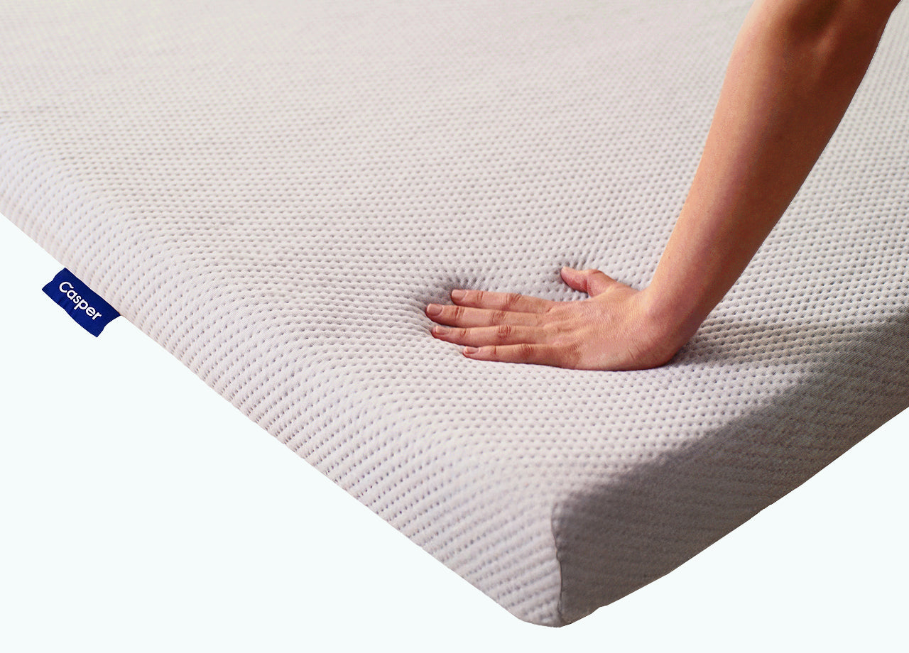 A person's hand presses down to feel the comfort of the Essential Topper.