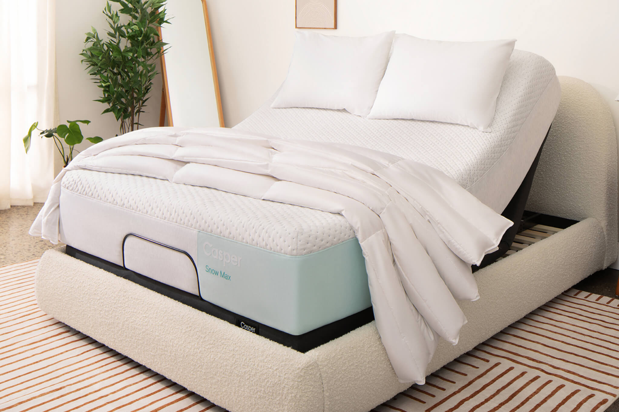 Image of an Adjustable Base with a mattress on top of it. The head of the base is raised, lifting up the head of the mattress for you to be lying upright in your bed. The mattress has two pillows and a folded blanket on top of it.