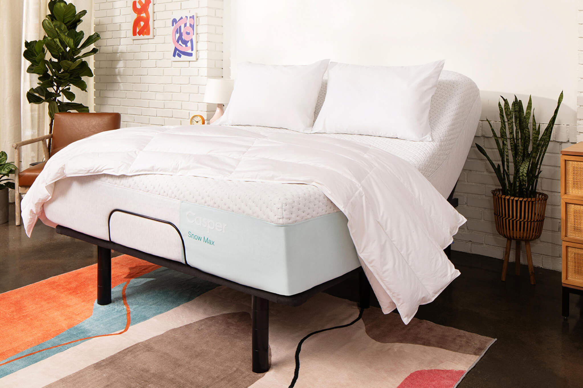 Image of an Adjustable Base with a mattress on top of it. The head of the base is raised, lifting up the head of the mattress for you to be lying upright in your bed. The mattress has two pillows and a folded blanket on top of it.