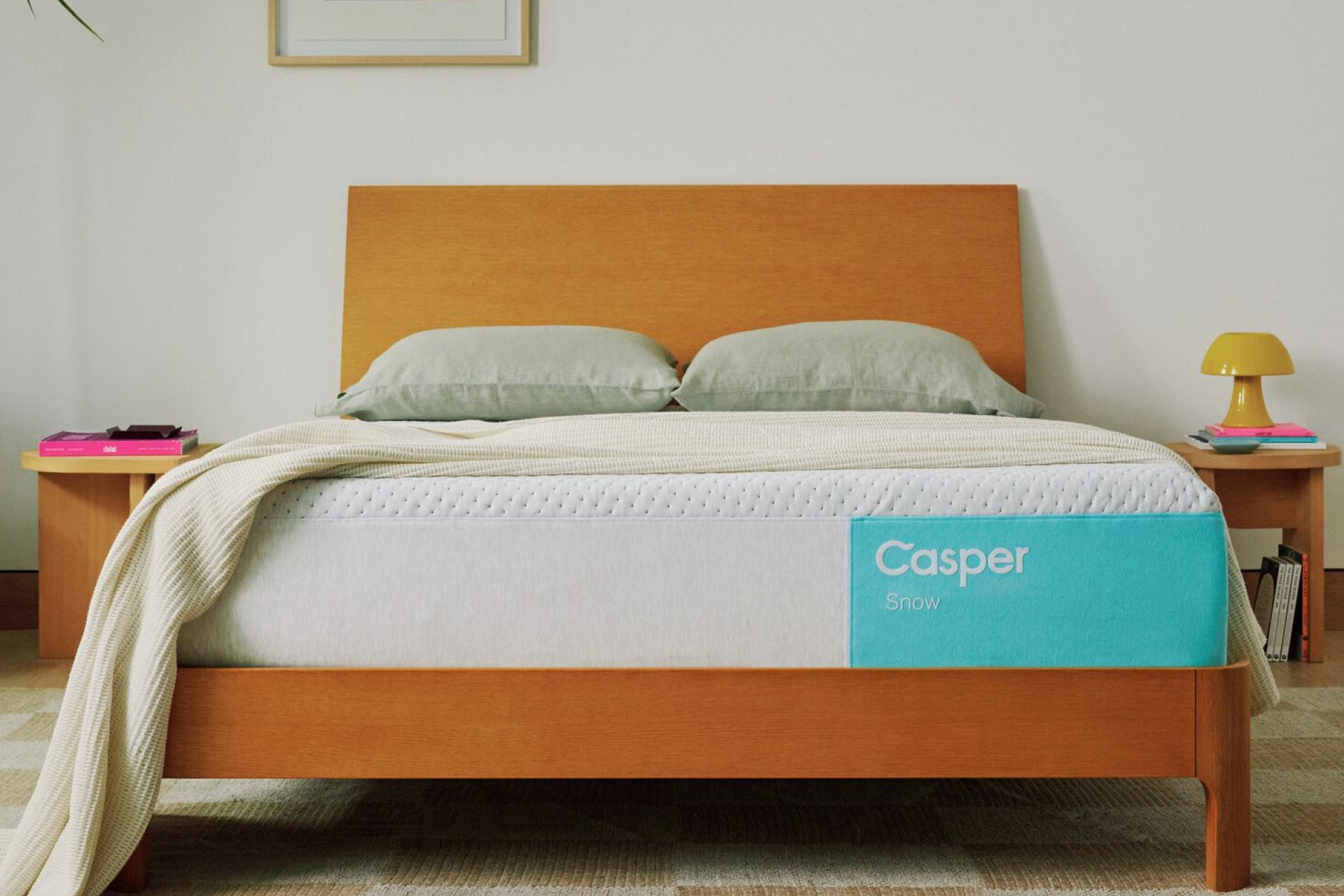 Casper's Snow mattress on a bed frame with pillows and a blanket folded on top.